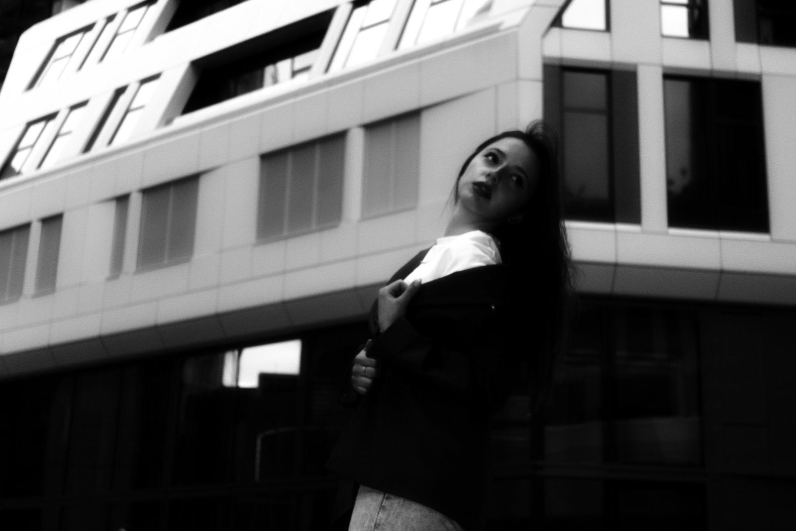 Schwarz-Weiß-Porträt einer Frau vor moderner Architektur, Blick über die Schulter