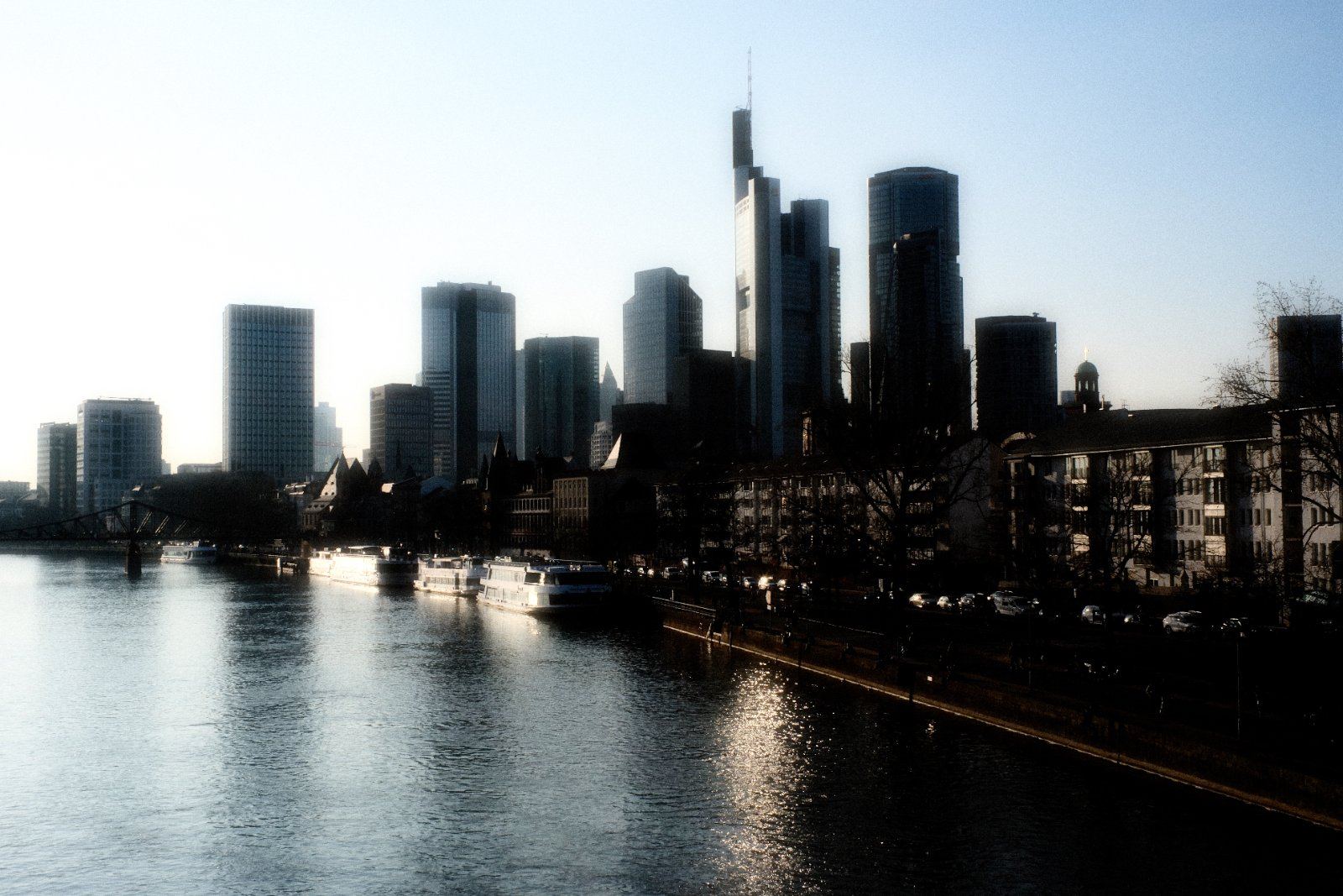 Frankfurter Skyline im Gegenlicht, gespiegelt im Main, mit Ausflugsschiffen am Ufer